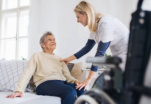 Pflegefachfrau kümmert sich um ältere Frau, die auf dem Bett sitzt