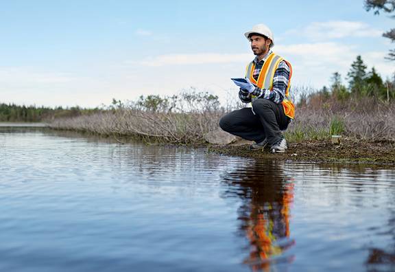 Mann analysiert Wasser und gibt Daten in sein Tablet ein