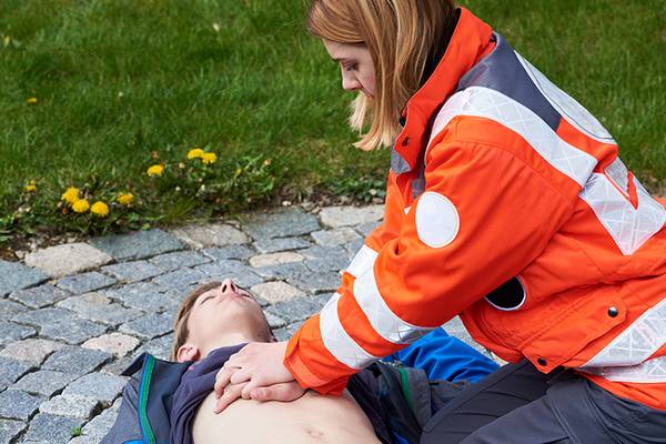 Junge Sanitäterin leistet erste Hilfe bei einem bewusstlosen jungen Mann