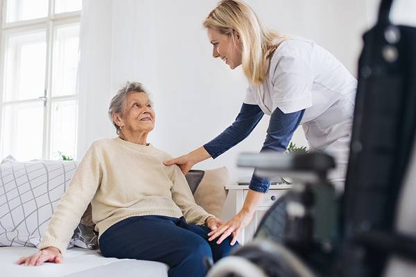 Pflegefachfrau kümmert sich um ältere Frau, die auf dem Bett sitzt